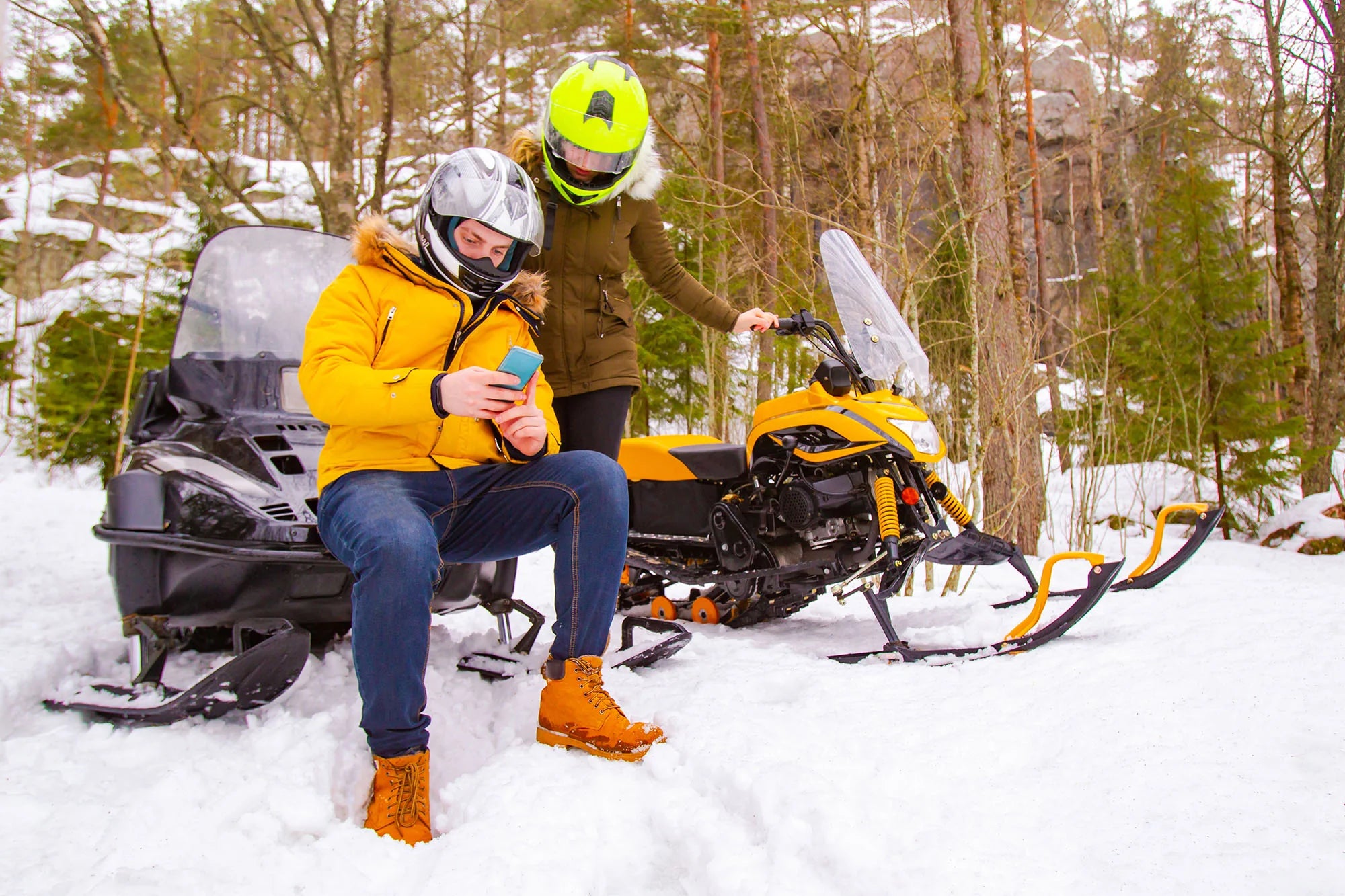 Snowmobiling couple taking a break to check the map on a cell phone