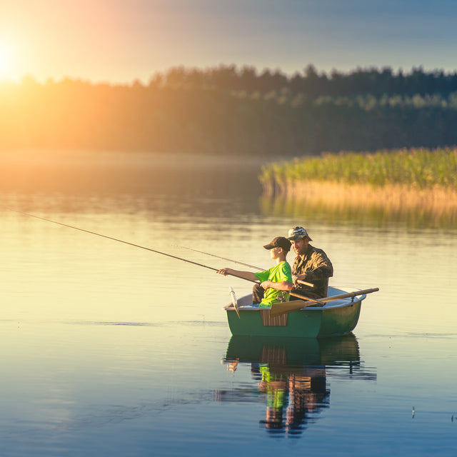 Father and son catching fish from a boat at sunset 