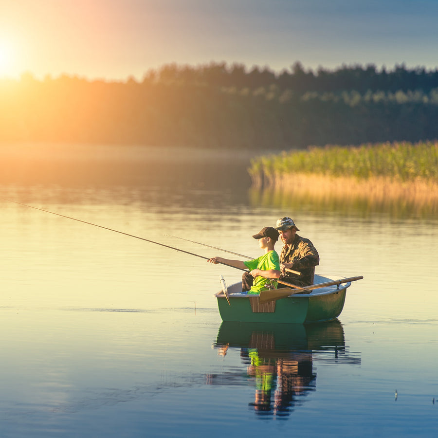 Father and son catching fish from a boat at sunset 
