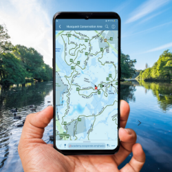 Hand holding smartphone displaying Avenza Maps App over background of a lake