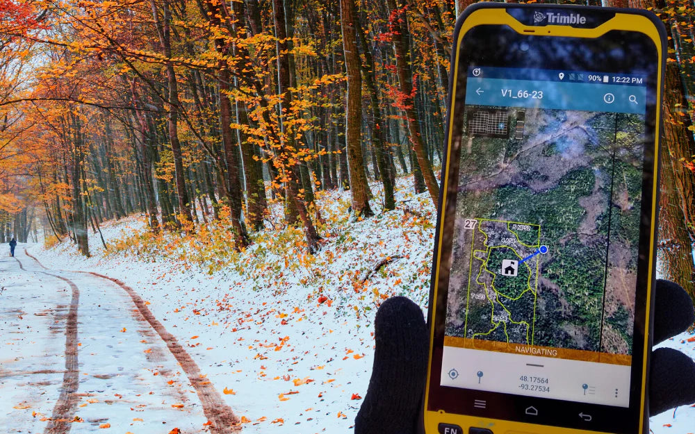 Trimble device with Avenza Maps app navigating on snow-covered trail through forest in autumn