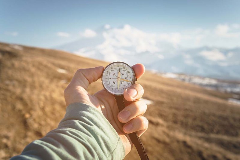 Hand holding compass against mountain scene