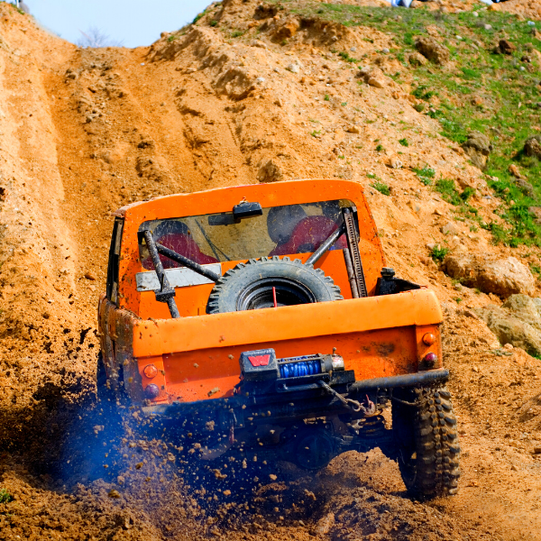 Orange off-roading vehicle driving up dirt hill