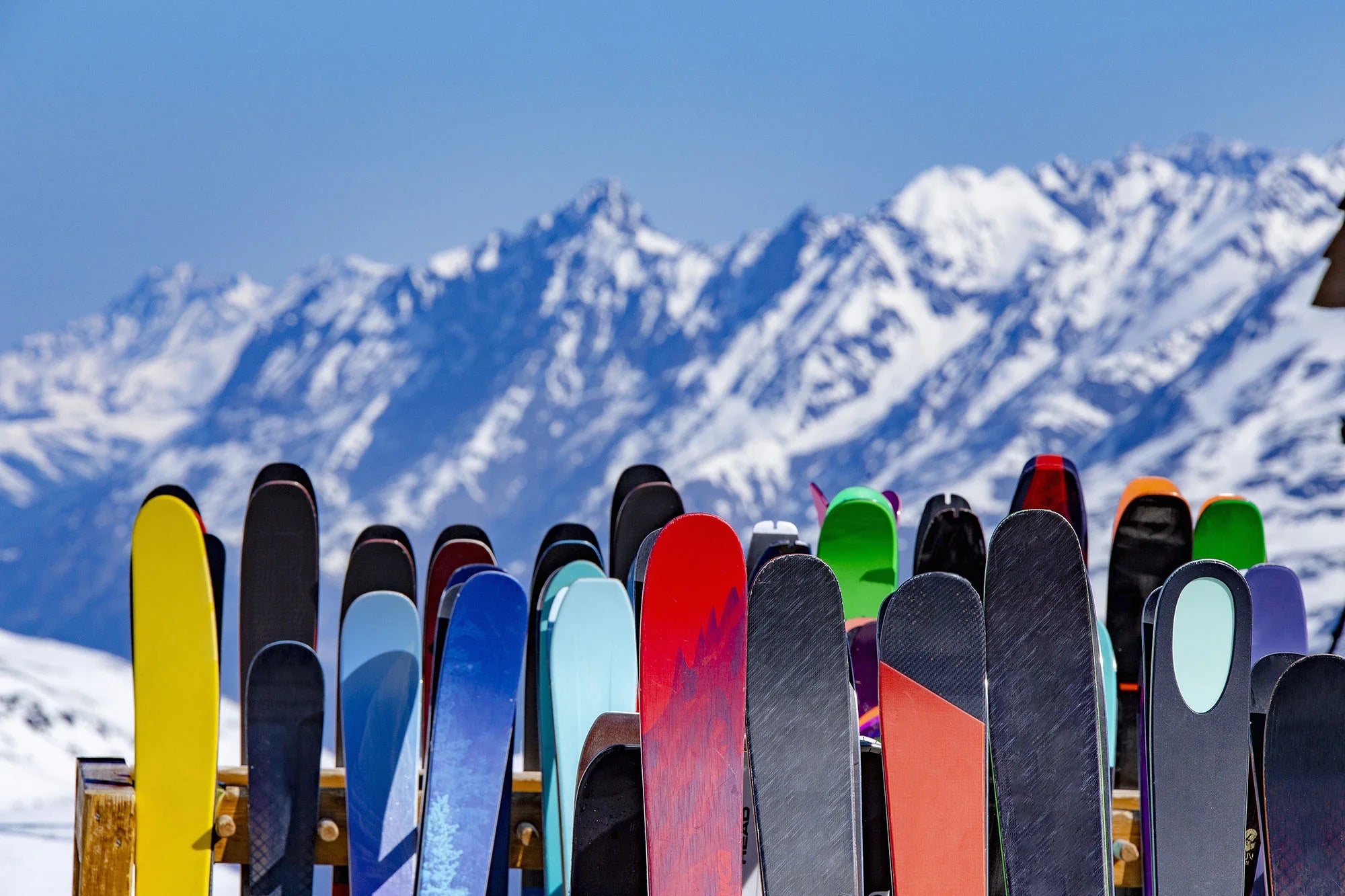 Colorful collection of skis on a ski rack with mountains in background
